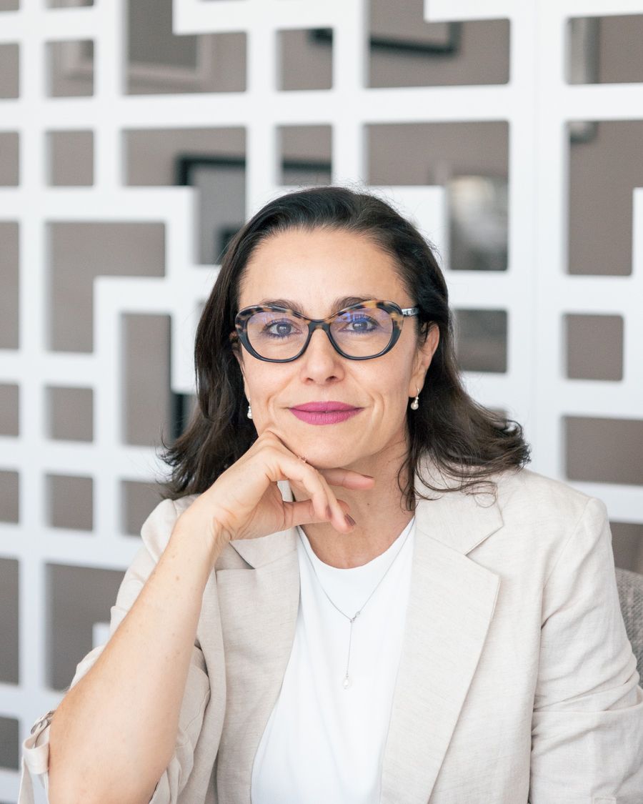 Retrato da Dra. Mônica Cereser, de óculos e blazer claro, sorrindo com a mão apoiada no queixo